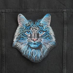 May include: Blue and white embroidered cat face patch. The cat has blue eyes and a pink nose.