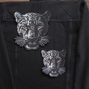 Op de afbeelding: Twee zwart-witte jaguar-patches genaaid op een zwart denim jack. De patches zijn gedetailleerd met witte vacht en zwarte vlekken.