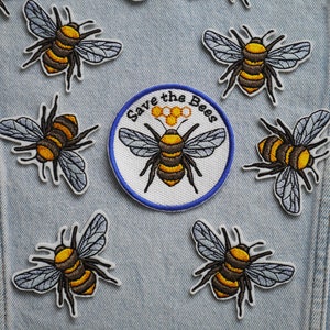 May include: A denim jacket with eight embroidered bee patches and one patch that says "Save the Bees" with a honeycomb design. The bees are yellow and black with grey wings.
