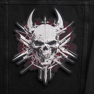 May include: Embroidered patch with a white skull design, horns, and a cross, set against a black background. The skull is surrounded by white and red jagged lines. The patch is designed for application on clothing or bags, with a gothic theme.