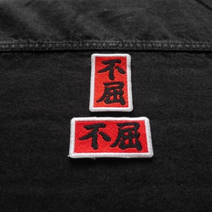 K&ouml;nnte beinhalten: Zwei rote gestickte Patches mit wei&szlig;en R&auml;ndern auf einer schwarzen Jeansjacke. Die Patches zeigen die chinesischen Schriftzeichen f&uuml;r "nicht betrunken".