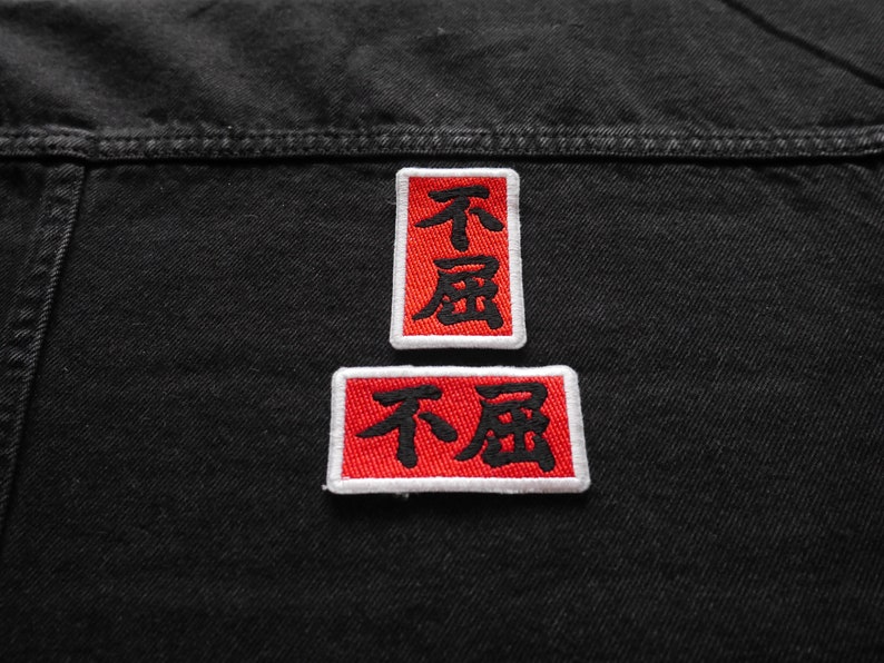 K&ouml;nnte beinhalten: Zwei rote gestickte Patches mit wei&szlig;en R&auml;ndern auf einer schwarzen Jeansjacke. Die Patches zeigen die chinesischen Schriftzeichen f&uuml;r "nicht betrunken".