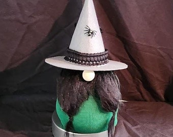 May include: A black and green witch gnome with a pointed hat and a black spider on the front. The gnome has a long black beard and a white face.