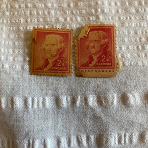 May include: Two vintage 2 cent US postage stamps featuring a portrait of Thomas Jefferson. The stamps are red and have a gold border. The stamps are slightly damaged.