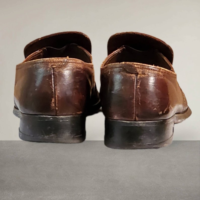 Puede incluir: Un par de zapatos de vestir marrones de cuero con suelas negras. Los zapatos est&aacute;n usados y tienen algunos rasgu&ntilde;os y marcas.