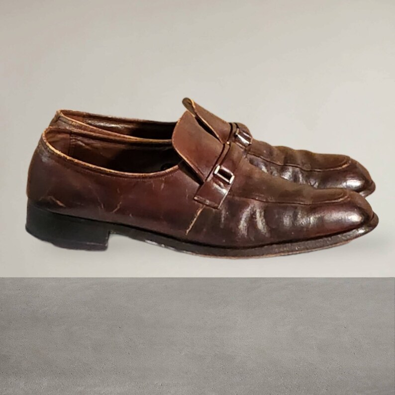 Puede incluir: Un par de zapatos marrones de cuero con cierre de hebilla. Los zapatos tienen un aspecto ligeramente desgastado y est&aacute;n hechos de cuero de alta calidad.