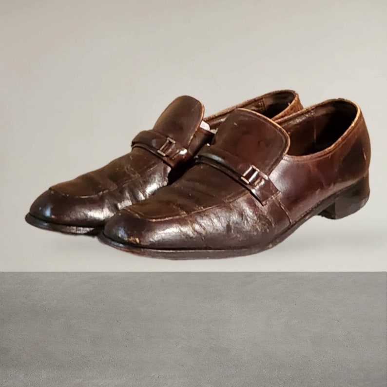 Puede incluir: Un par de zapatos de vestir de cuero marr&oacute;n con una correa de hebilla sobre el empeine.