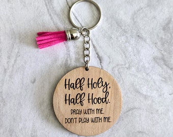 Può includere: Un portachiavi in legno con un fiocco rosa. Il portachiavi ha il testo "Half Holy. Half Hood. Pray with me. Don't play with me."