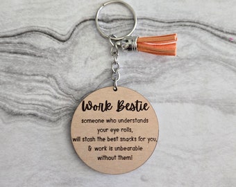Può includere: Un portachiavi in legno con un'etichetta rotonda che dice "Work Bestie someone who understands your eye rolls, will stash the best snacks for you, & work is unbearable without them!"
