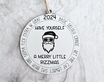 Può includere: Un addobbo natalizio rotondo bianco con un'illustrazione in bianco e nero di Babbo Natale con occhiali da sole. L'addobbo ha il testo "2024 HAVE YOURSELF A MERRY LITTLE RIZZMAS" attorno al bordo.