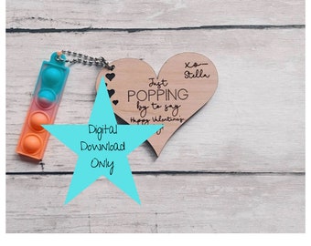 Puede incluir: Un adorno de madera en forma de corazón con el texto "Just Popping by to say Happy Valentine's" y "xo-Stella". El adorno está unido a una cadena con un juguete pop-it colorido.