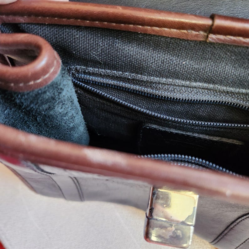 May include: The inside of a brown leather purse with a black canvas lining. The purse has a zippered pocket and a flap closure with a metal clasp.