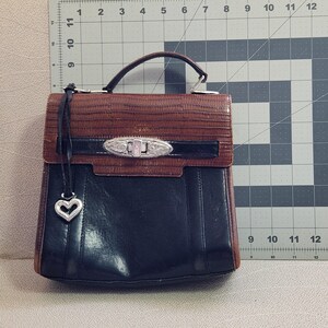 May include: A brown and black leather satchel handbag with a silver heart charm and a silver lock and key closure.