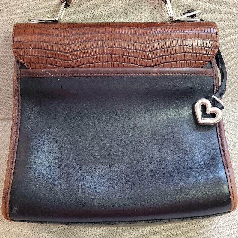 May include: A black leather handbag with a brown leather flap and a silver heart charm.
