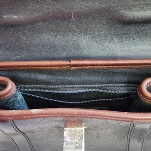 May include: The inside of a brown leather briefcase with a black zippered pocket and a silver clasp.