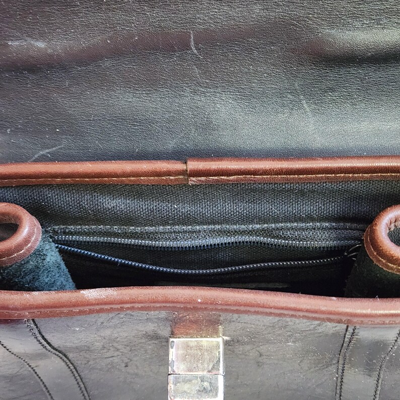 May include: The inside of a brown leather briefcase with a black zippered pocket and a silver clasp.