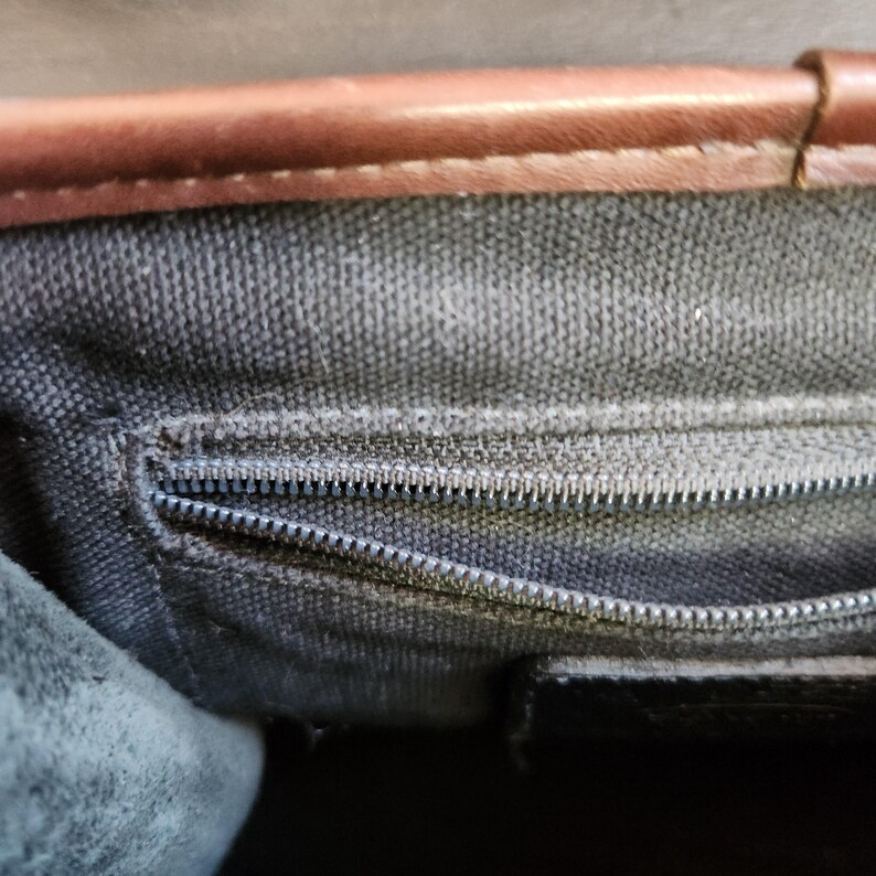 May include: Close-up of a brown leather bag with a black zipper and a black canvas lining.