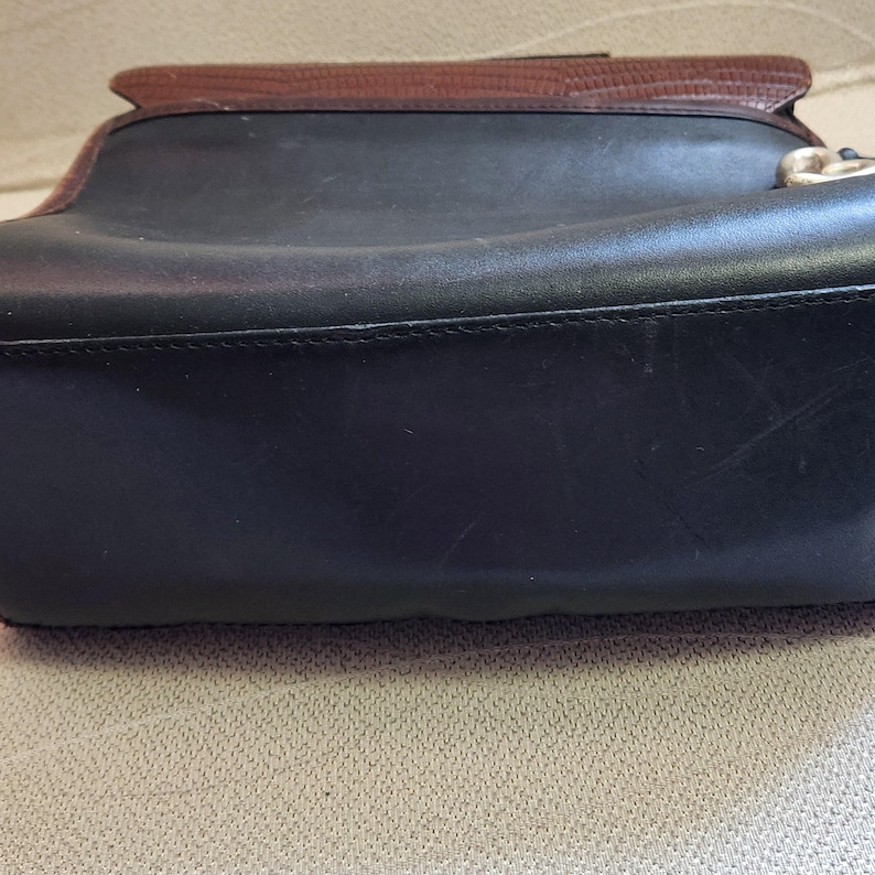 May include: Close-up of the bottom of a black leather handbag with brown leather trim. The bag has a stitched seam around the edge.