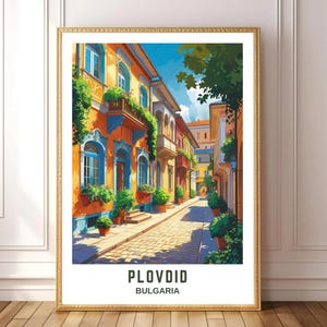 May include: A framed art print featuring a vibrant street scene in Plovdiv, Bulgaria. The artwork depicts colorful buildings with orange, blue, and yellow facades, lush greenery, and cobblestone streets. The text "PLOVDIV BULGARIA" is at the bottom.