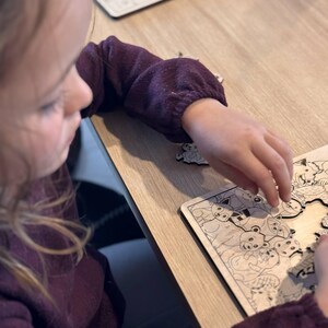 K&ouml;nnte beinhalten: Ein junges Kind arbeitet an einem Holzpuzzle mit verschiedenen Tieren. Die Puzzleteile liegen auf dem Tisch verstreut, und das Kind setzt vorsichtig ein Teil in das Puzzle ein.