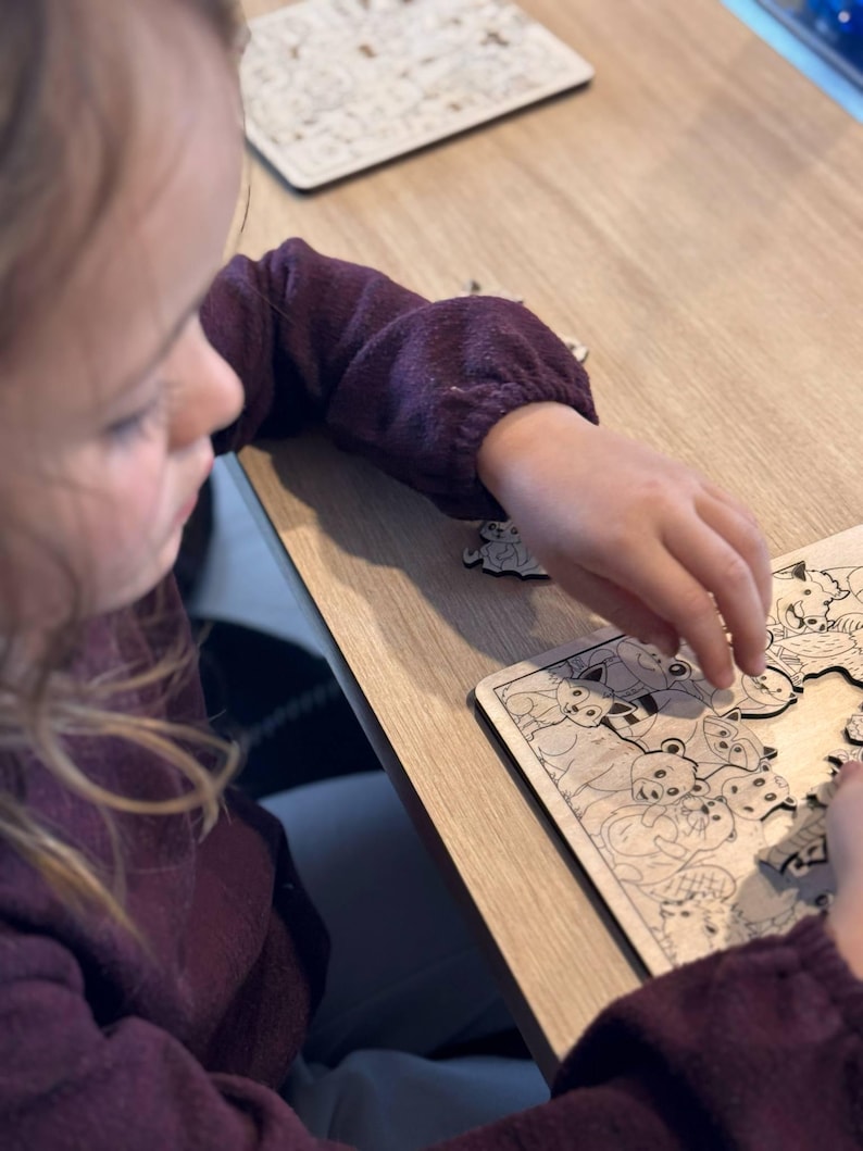 K&ouml;nnte beinhalten: Ein junges Kind arbeitet an einem Holzpuzzle mit verschiedenen Tieren. Die Puzzleteile liegen auf dem Tisch verstreut, und das Kind setzt vorsichtig ein Teil in das Puzzle ein.
