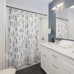 May include: A white shower curtain with a black and white bunny rabbit pattern. The shower curtain is hanging in a bathroom with a white vanity and a mirror.