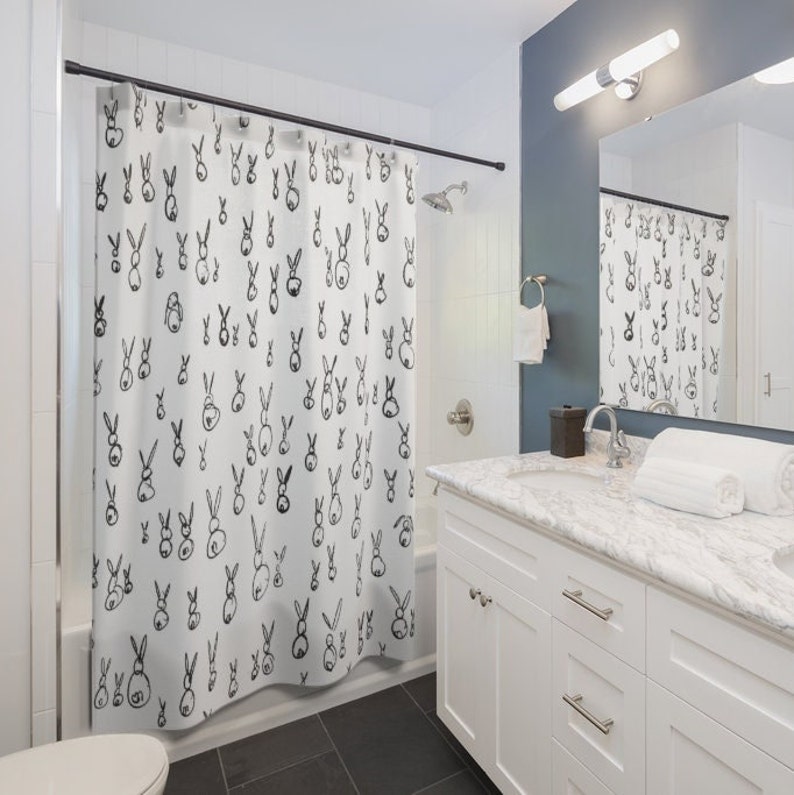 May include: A white shower curtain with a black and white bunny rabbit pattern. The shower curtain is hanging in a bathroom with a white vanity and a mirror.
