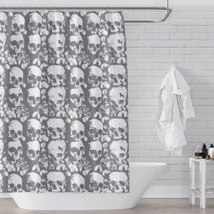 May include: A grey shower curtain with a white skull pattern. The shower curtain is hanging in a bathroom with a white brick wall and a white towel hanging on a hook.