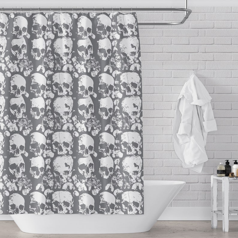 May include: A grey shower curtain with a white skull pattern. The shower curtain is hanging in a bathroom with a white brick wall and a white towel hanging on a hook.