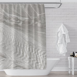 May include: A gray shower curtain with a subtle, textured pattern. The curtain is hanging in a bathroom with a white brick wall and a white bathtub.