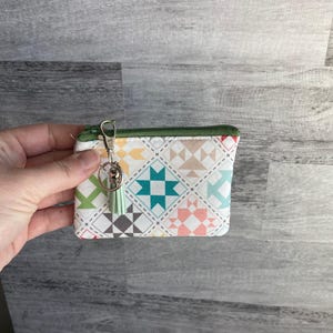 May include: A small white zippered pouch with a colorful patchwork design. The pouch has a green tassel attached to a silver key ring.