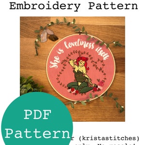Puede incluir: Un aro de bordado rosa con una imagen bordada en verde y rojo de Poison Ivy de DC Comics. El bordado incluye el texto "She is loveliness itself".
