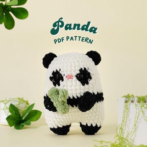 May include: A crocheted panda amigurumi toy holding a green bamboo shoot. The panda is white with black eyes, nose, and ears. The toy is sitting on a white surface with green foliage in the background. The text "Panda PDF Pattern" is written in green letters above the toy.