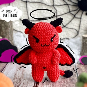 Puede incluir: Un juguete de peluche de diablo rojo tejido a crochet con cuernos, alas y cola negros. El juguete tiene un halo sobre su cabeza y un globo de pensamiento que dice "PDF PATTERN".