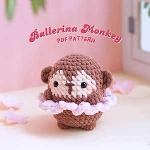 May include: A brown and white crocheted monkey wearing a pink tutu. The monkey is a ballerina monkey and the image includes the text "Ballerina Monkey PDF Pattern".