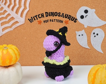 May include: A purple crocheted dinosaur wearing a black witch hat with a yellow star, a black cape, and a green collar. The dinosaur is sitting on a white surface in front of a brown corkboard with white ghosts and orange pumpkins.