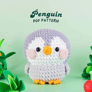 Könnte beinhalten: Ein handgefertigter, grau-weißer Häkelpinguin mit gelbem Schnabel und Füßen sowie rosa Wangen. Der Pinguin ist ein weiches, plüschiges Spielzeug. Das Bild enthält den Text "Penguin PDF PATTERN" in grüner, kursiver Schrift.