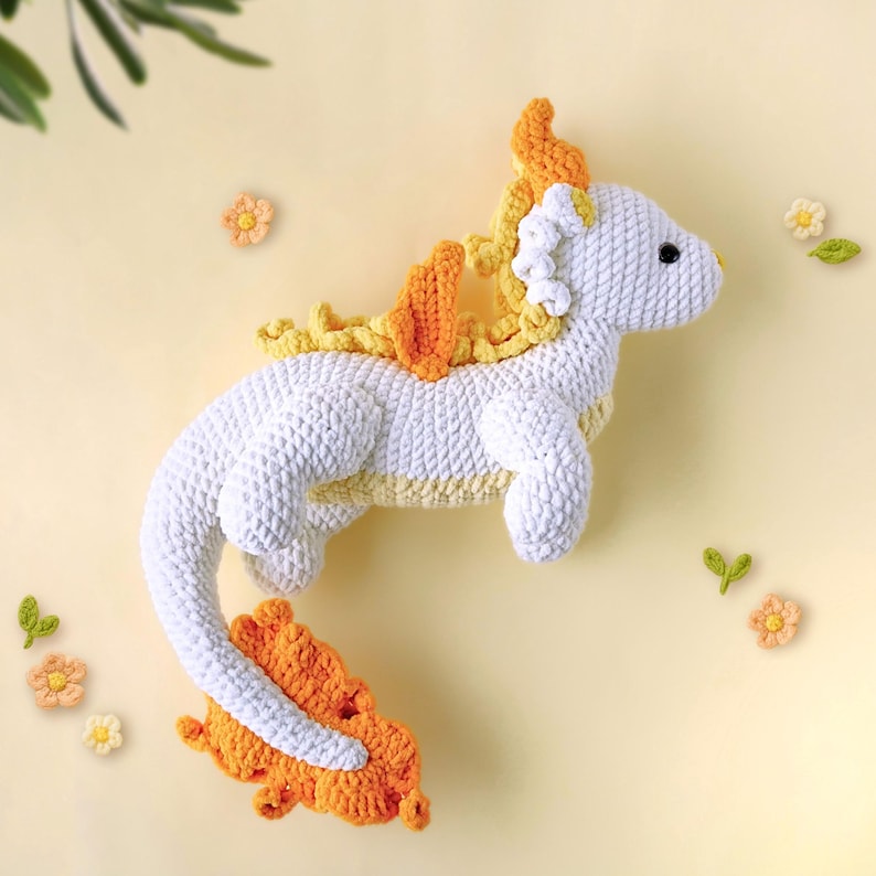 May include: A white crocheted dragon with a yellow and orange tail and mane. The dragon is a plush toy.