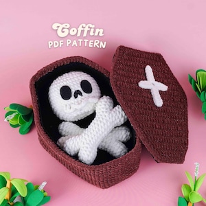 May include: A crocheted coffin with a white skull and crossbones inside, with the text "Coffin PDF Pattern" in a whimsical font. The coffin is brown with a white cross on the lid, set against a pink background.