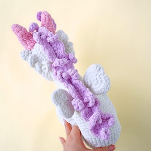 May include: White crocheted unicorn stuffed animal with a pink and purple mane and tail. The unicorn has wings and is standing on its hind legs.