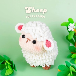 Op de afbeelding: Een handgemaakt schapenknuffel met witte, pluizige wol, roze oren en een lichtbruin gezicht. De tekst "Sheep PDF Pattern" staat bovenaan. Groene decoratieve bladeren en bloemen zijn op de achtergrond.