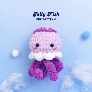 May include: A crocheted jellyfish toy in purple, lilac, and white, with black eyes and a smiling mouth. The text "Jelly Fish PDF PATTERN" is displayed above the jellyfish on a light blue background.