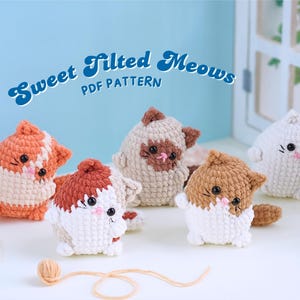 May include: Four crocheted cat amigurumi toys with tilted heads. The cats are white with brown, orange, and beige accents. The toys are sitting on a light blue surface with a white wooden background. The text "Sweet Tilted Meows PDF Pattern" is written in blue and white on the background.