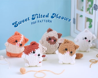 May include: Four crocheted cat amigurumi toys with tilted heads. The cats are white with brown, orange, and beige accents. The toys are sitting on a light blue surface with a white wooden background. The text "Sweet Tilted Meows PDF Pattern" is written in blue and white on the background.