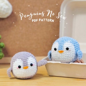 May include: Two crocheted penguin amigurumi toys. One penguin is light blue and white, the other is gray and white. Both penguins have black eyes and orange beaks. The text "Penguins No Sew PDF Pattern" is written above the penguins.