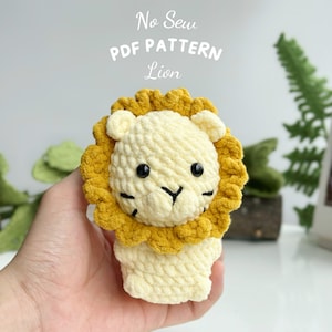 May include: A crocheted lion toy with a yellow mane and white body. The toy is being held in a hand. The image text reads "No Sew PDF PATTERN Lion".