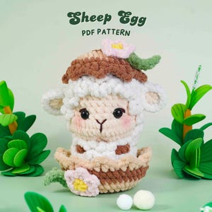 May include: A crocheted sheep-shaped egg with a brown and white shell, decorated with pink and green floral details. The text "Sheep Egg PDF PATTERN" is above the egg. Green foliage surrounds the egg.