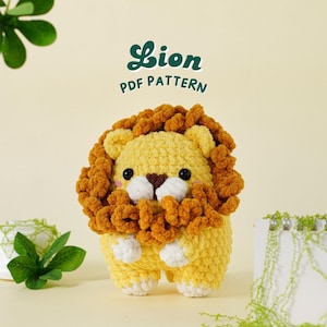 May include: A crocheted lion amigurumi toy with a yellow body and brown mane. The toy has a cute face with black eyes and a white nose. The toy is sitting on a white surface with green plants in the background. The text "Lion PDF Pattern" is written in green letters on a white background.