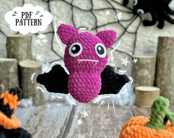 May include: A crocheted purple bat with black wings and white eyes. The bat is holding a small white sign that says "PDF PATTERN".