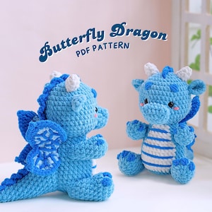 Könnte beinhalten: Zwei gehäkelte blaue Schmetterlingsdrachen-Amigurumi-Spielzeuge. Der Drache links hat Flügel und einen langen Schwanz. Der Drache rechts hat einen gestreiften Körper. Der Text "Butterfly Dragon PDF Pattern" befindet sich oben im Bild.